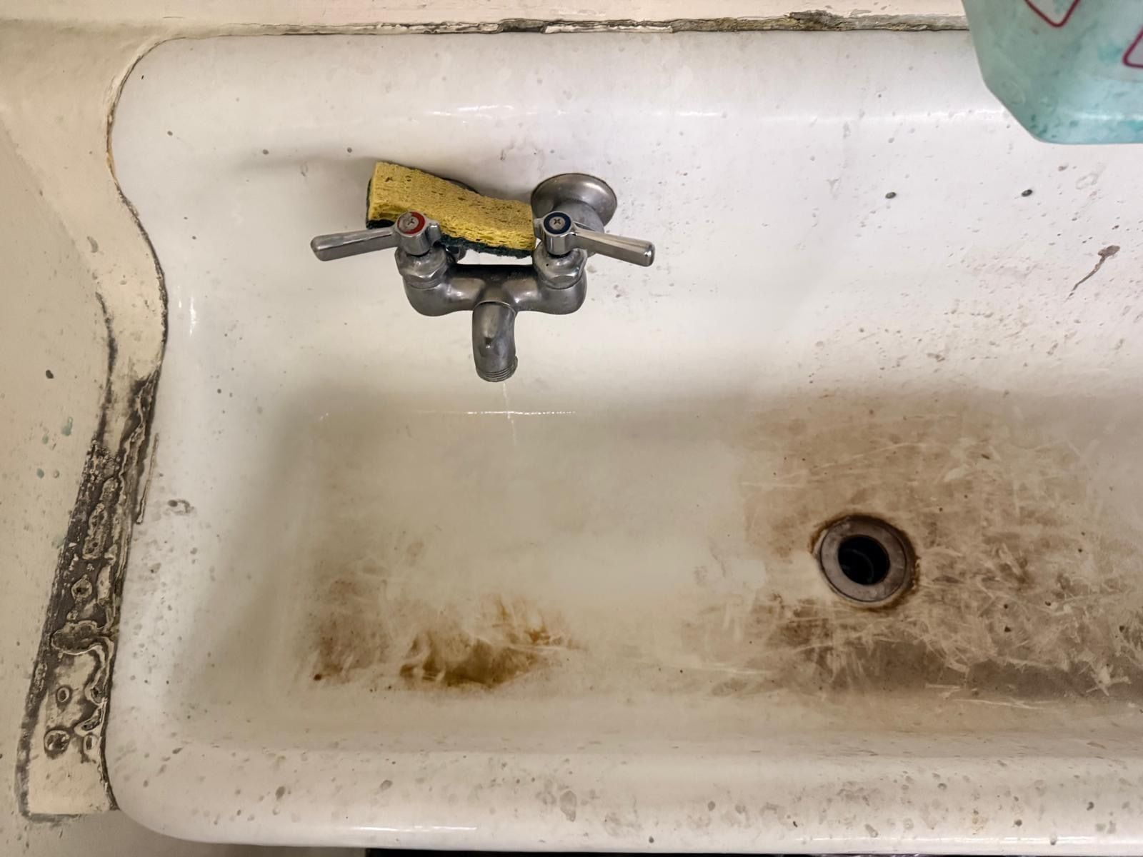 A white utility sink with brown stains and scuff marks around the drain